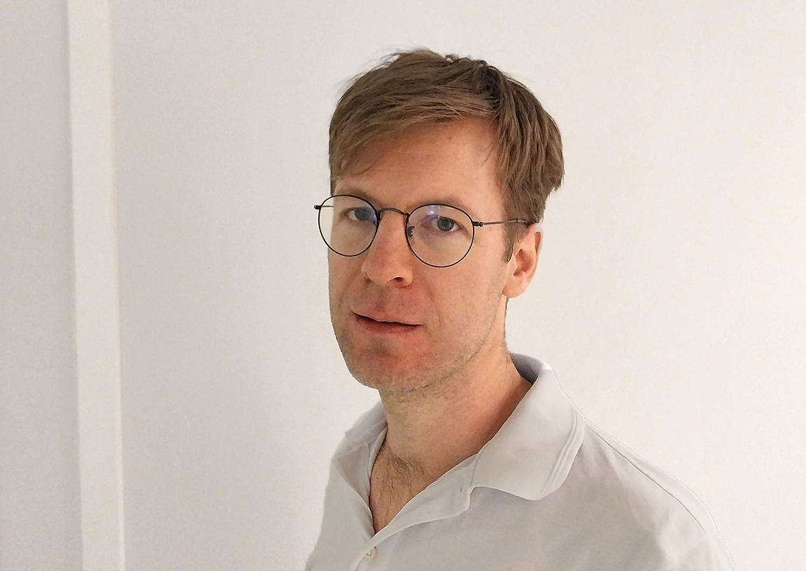 Porträttbild Jakob Nissen i vit pikétröja, kort hår med sidbena och runda glasögon.